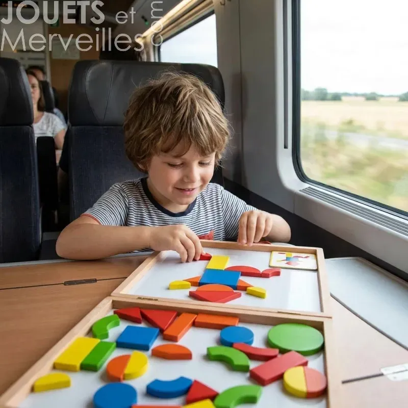 Enfant assis près de la fenêtre dans un train, jouant avec des formes géométriques colorées en bois sur une table.
