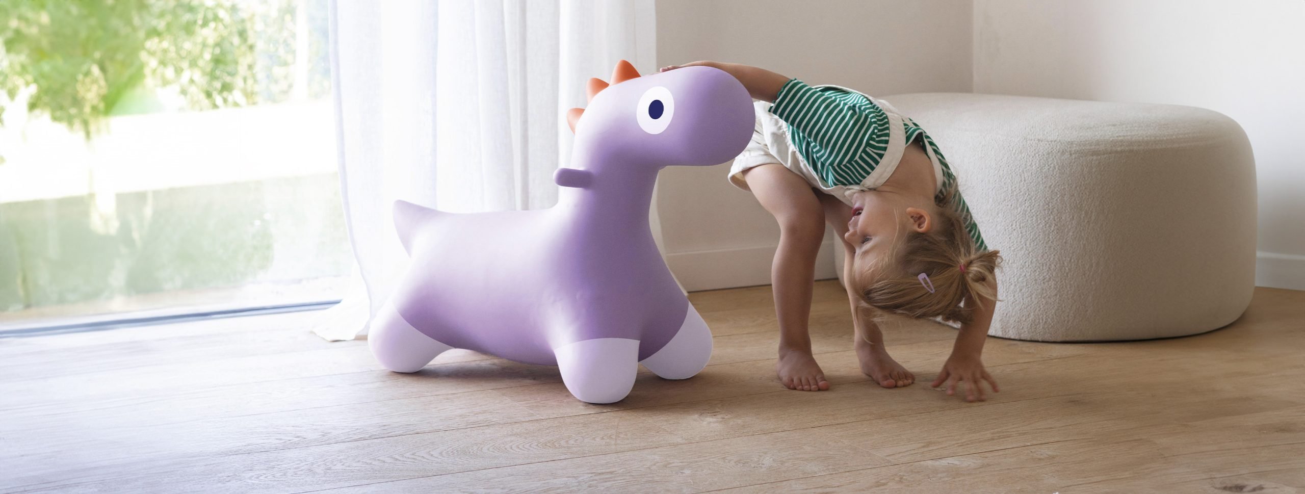Enfant jouant avec un animal sauteur Quut en forme de poney violet gonflable, dans une pièce lumineuse.