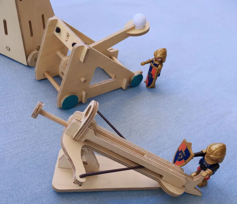 Figurines et jouets en bois: catapulte et trébuchet miniatures en bois, avec chevaliers miniatures près d’eux sur fond bleu.