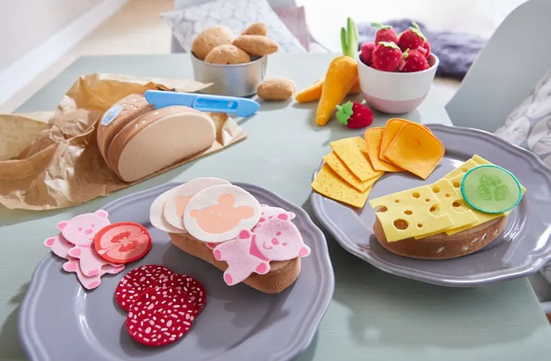 Gamme de nourriture jouet colorée: sandwiches en feutrine avec fromages et tranches décoratives, et salade de fruits en mousse sur assiettes.