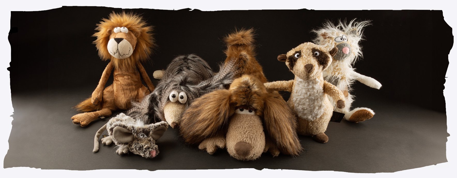 Groupe de peluches et marionnettes soft, dont un lion, un chien et d’autres animaux à poils longs, posés sur fond sombre.