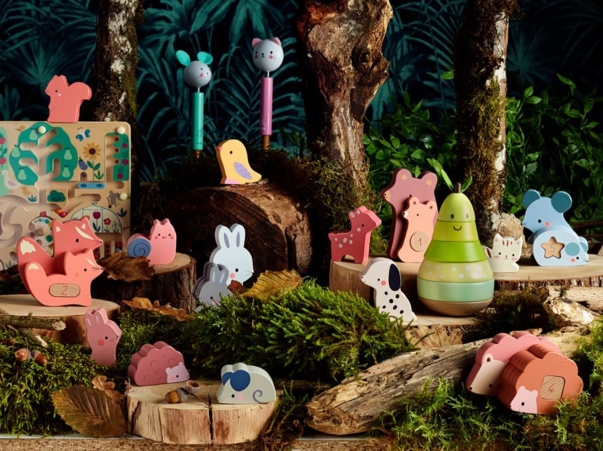 Décor forestier avec jouets colorés en bois: animaux et peluches pastel, puzzles, poupées et figurines sur troncs et mousse.