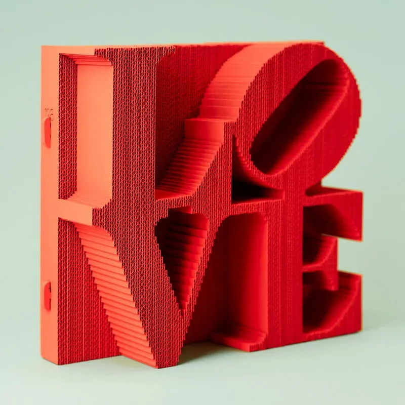 Lettrage 3D en forme de mot “LOVE” en rouge corail, structure plissée et effet en relief, posé sur fond vert pâle.