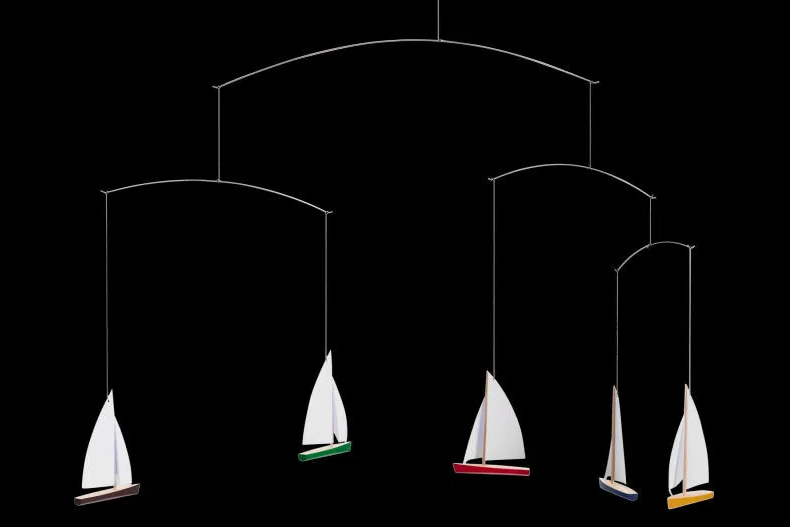 Mobile décoratif avec plusieurs voiliers miniatures suspendus contre fond noir. Chaque voilier a une coque colorée et voile blanc.
