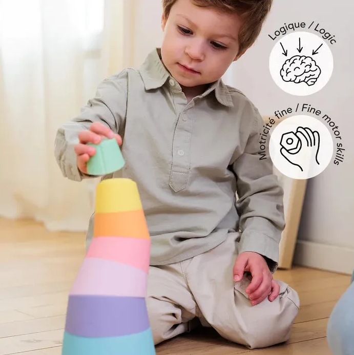 Petit garçon jouant avec des cônes colorés, empilement d’un motif arc-en-ciel; jeu favorise la logique et les compétences motrices fines.
