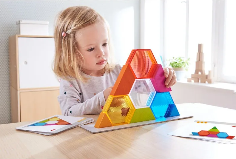 Petite fille jouant avec un pyramidage magnétique coloré en forme d’hexagones sur une table, avec des fiches d’activités à côté.