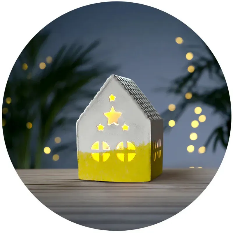 Petite maison décorative lumineuse Mako Moulage en plâtre blanche et jaune, illuminant l’intérieur à travers les fenêtres et le toit, ambiance chaleureuse.
