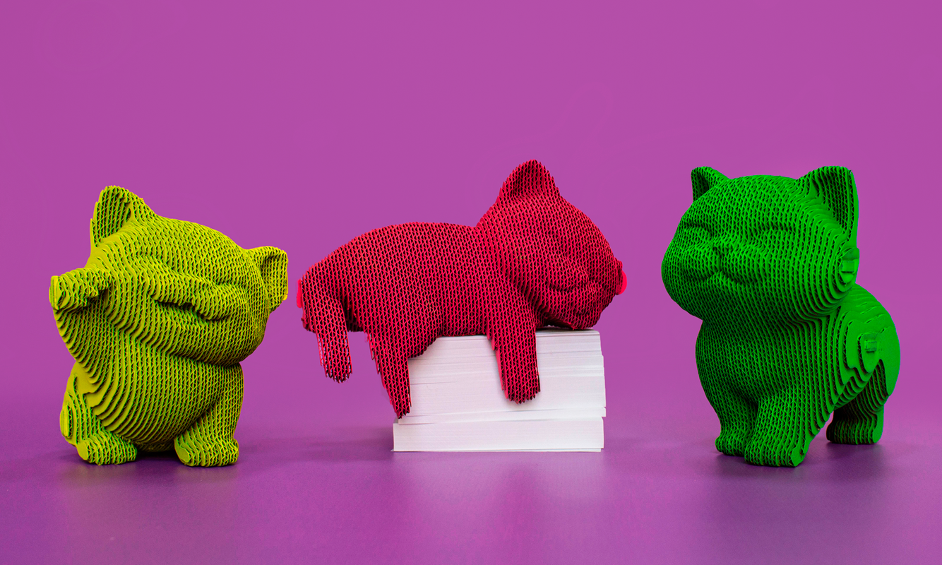 Trois figurines cartonnées en forme d’animaux colorés (jaune, rouge, vert) alignés autour d’un petit tas de livres blanc sur fond violet.